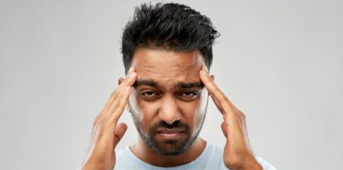 A man holding his hands on either side of his head, as if he is experiencing migraine pain.